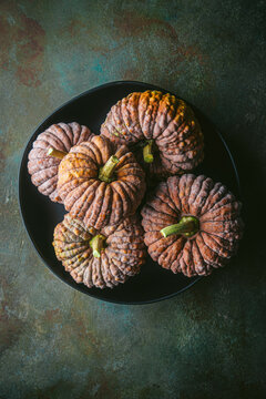 Arrangement of 5 heirloom pumpkins in black bowl with custom teal and copper background