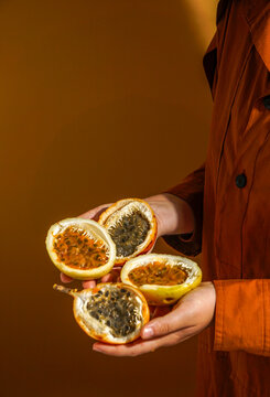 hand holding freshly cut passion fruit (Passiflora edulis and Passiflora ligularis), revealing its vibrant, juicy orange pulp filled with glossy seeds