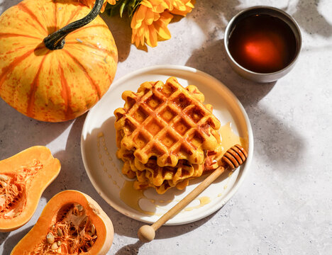 pumpkin waffles drizzled with honey on a white plate, surrounded by autumn-themed decorations including a whole pumpkin