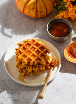 pumpkin waffles drizzled with honey on a white plate, surrounded by autumn-themed decorations including a whole pumpkin