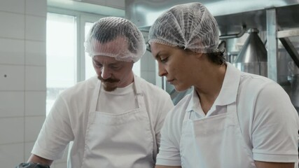 Tilting medium closeup of hands and faces of Caucasian male and female factory staff shredding pressed cooked curd into pieces for making stretched artisan Italian cheese