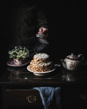 Moody scene with an Almond Cake as a hero dessert. Background with flowers , a teapot and  a blue linen  over a vintage table.