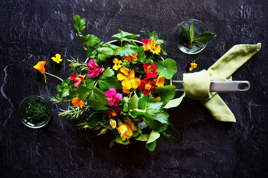 Cooking with herbs and edible flowers concept. Frypan skillet on dark background.