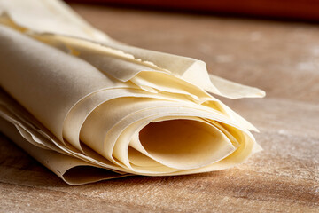 On a wooden cutting board, rolled layers of phyllo dough are arranged diagonally, creating an interplay of textures and transparencies.