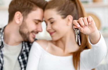 First home for young family. Happy husband and wife in living room interior, woman shows keys, close up, panorama