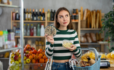 Preparing for Christmas celebration - girl chooses salted herring in produce section of the supermarket
