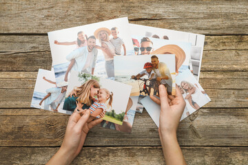 Woman with different photos in open photo album at wooden table, top view