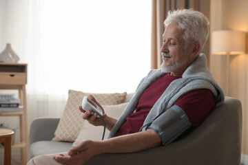 Senior man measuring blood pressure on sofa indoors