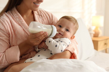 Mother feeding her little baby from bottle on bed at home, closeup