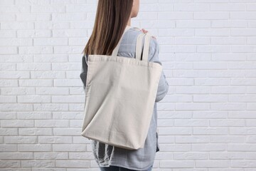 Woman with blank shopper bag near white brick wall, back view. Mockup for design