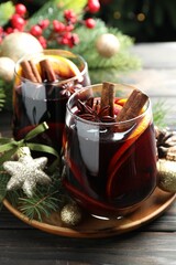Tasty mulled wine with spices and Christmas decor on wooden table, closeup