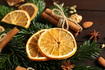 Different spices, dried orange slices and fir tree branches on wooden table, closeup. Christmas season