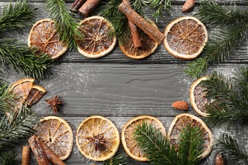 Frame of different aromatic spices and fir tree branches on grey wooden table, flat lay with space for text. Christmas season