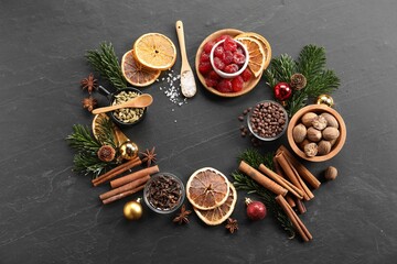 Frame of different aromatic spices and fir tree branches on black table, flat lay. Christmas season