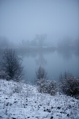 Landscape on the frozen river , cold picture.Christmas mood in the photo.Frozen lake covered by snow around,reflections on water.Foggy and misty weather on the lake ,blue colors,clouds in the sky 