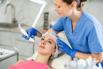 Beautician in gloves use macromolecule atomizing pen for atomized nutrients to supplement, face skin nutrition young girl in cosmetology clinic. Professional moisturizing and rejuvenating hardware