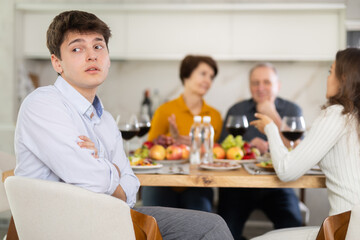 Upset young guy at family holiday table with parents at home. Unpleasant discussion