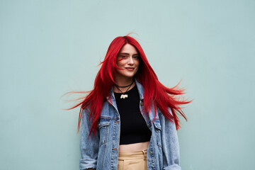 Young woman with vibrant red hair poses casually against a light blue wall