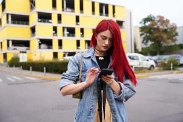 Fototapeta premium Young woman with red hair checks phone while walking through parking lot