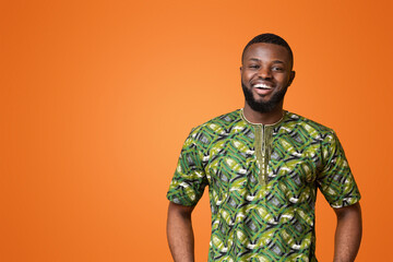 Confident black man in green african costume posing over yellow studio background