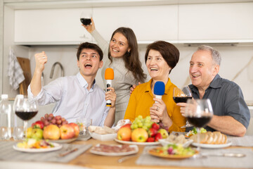 Friendly family with adult children singing karaoke together at home