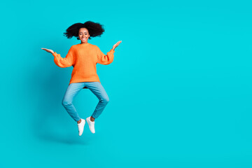 Full body photo of attractive young woman jump compare empty space dressed stylish knitted orange clothes isolated on cyan color background
