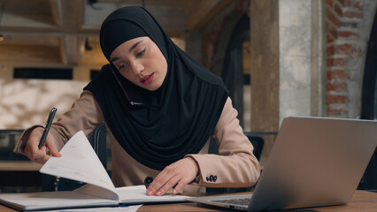 Muslim woman in hijab female office manager businesswoman consult client talk mobile phone at business company Arabian islamic girl freelancer student working with laptop computer write notes at cafe