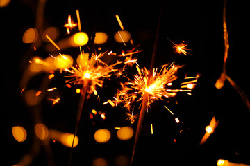 Obraz premium Sparkling shining fireworks with gold glitter and bokeh on black background.Sparkler Fireworks with Bokeh Effect.Close-Up of Sparklers Against Dark Background.Sparklers with Bokeh Lights at Night