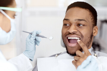 Black Male Patient Showing Aching Tooth During Check Up With Female Dentist, Young African American...