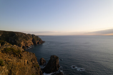 Coastal landscape at dusk with rocky cliffs and calm ocean waters