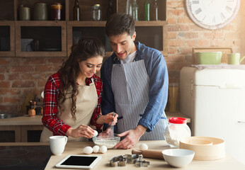 Happy young woman and man baking pie in loft kitchen. Young family cooking at home, using digital...