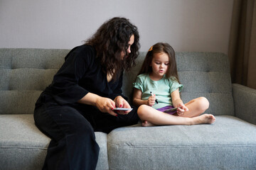 Mother and daughter engaging in creative play on a cozy gray couch at home