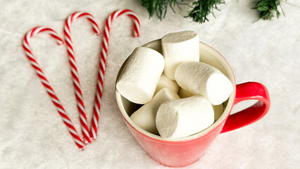 Cup of hot drink with marshmallow, gingerbread cookie and candy cane on table. Christmas food and drink concept.