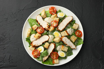 Tasty Caesar salad with chicken and tomatoes on black table, top view