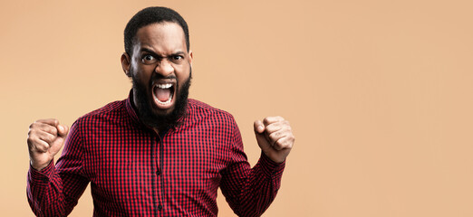 Human Emotions, Facial Expression Concept. Close up portrait of african man screaming with clenched fists, yellow studio