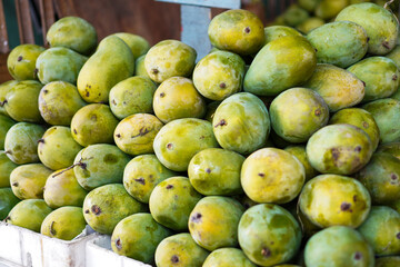 Close-up view of a pile of green mangoes at a market. The mangoes are fresh and look ready to be purchased. Fresh Green Mangoes at a Market Stall.