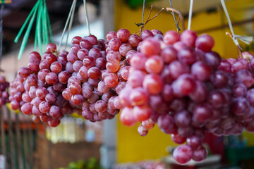 Close-up of bunches of ripe red grapes hanging at a market stall. The grapes are vibrant and appear juicy and fresh. Vibrant Red Grapes Hanging at a Market.