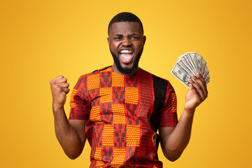 Happy african american guy in traditional t-shirt holding bunch of money and shouting, yellow...