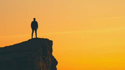 A silhouetted figure stands on a cliff at sunset, enjoying a breathtaking view of the vibrant orange sky.