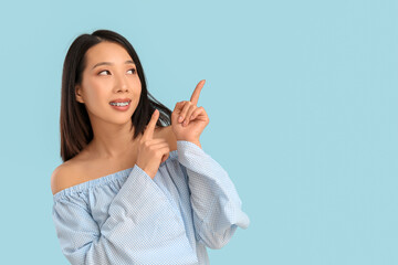 Portrait of pretty young Asian woman pointing at something on blue background