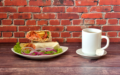 Delicious juicy meat shawarma with lettuce and red onion on a wooden table, next to a cup of hot tea.