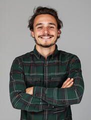 Cheerful young man in plaid shirt smiling with arms crossed in studio