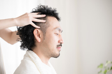  目を閉じる男性のヘッドマッサージやヘッドスパなどをするイメージ...
