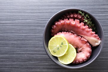 Fresh raw octopus, lemon and thyme in bowl on dark textured table, top view. Space for text