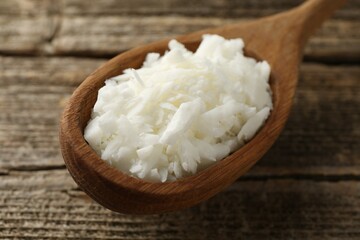 White soy wax flakes in spoon on wooden table, closeup