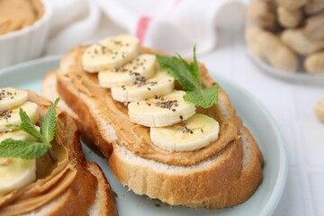 Tasty sandwiches with peanut butter, banana, chia seeds and mint on table, closeup