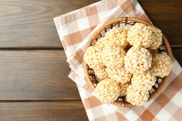 Tasty puffed rice balls in wicker basket on wooden table, top view. Space for text