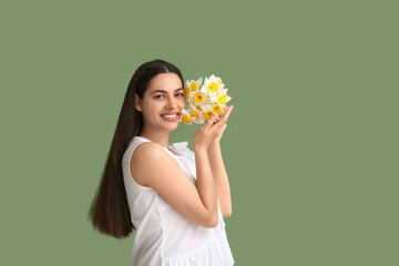 Beautiful young woman with bouquet of daffodil flowers on green background