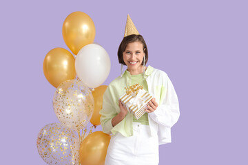 Beautiful woman in party hat with Birthday gift and balloons on lilac background