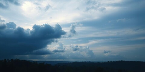 A moody scene featuring a cloudy blue sky with a large texture cloud casting a gloomy atmosphere over the land with trees and hills stretching out in the distance, blue sky, nature, tree lines